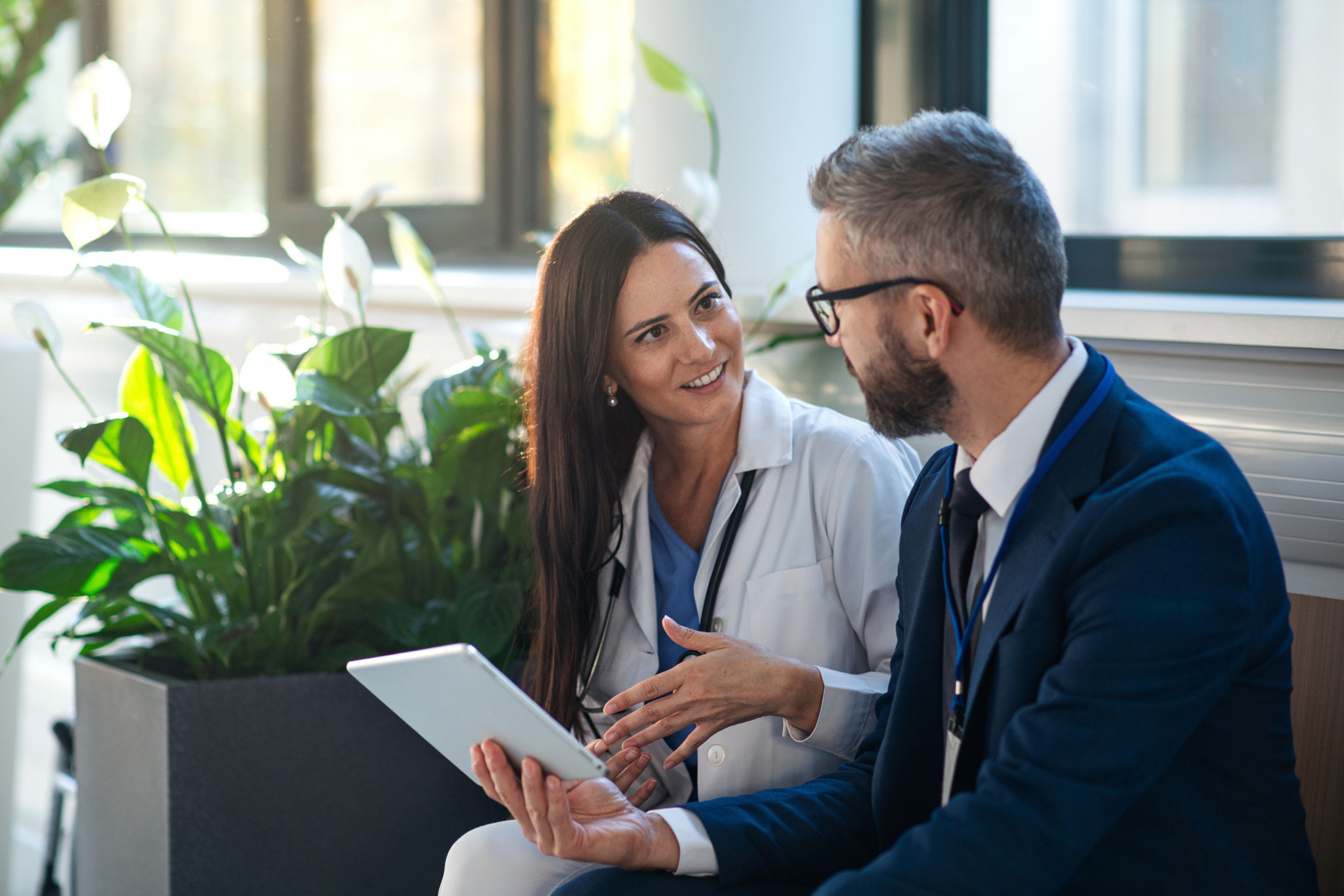 M&eacute;decin en blouse blanche &eacute;changeant avec un consultant Forvis Mazars autour d'une tablette