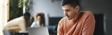 Employee typing on his laptop while sitting at the office desk. Man in jumper filing his tax returns on computer.