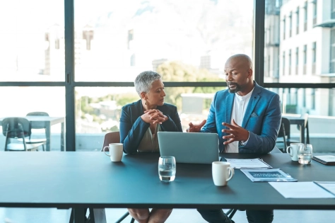 2 people sitting and looking at a laptop while explaining something