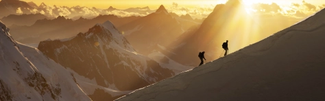 Climbers on a snowy ridge at sunrise ascending the Monte Rosa. On the background the Matterhorn.