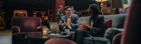 Smiling male professional discussing with female colleague sitting in hotel lounge