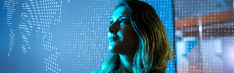 Mature business woman with blonde hair staring at a digital hologram of the world map. Future of digital technology and business innovation.