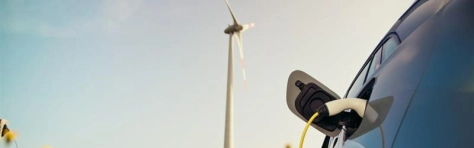 macchina elettrica che si ricarica con nello sfondo una pala eolica