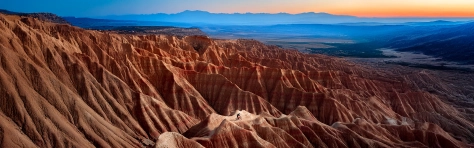 Wide panoramic landscape of desert rock formations at sunrise with dramatic light and horizon view.