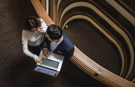 Two people standing next to the rail. One of them is holding laptop and showing something on the screen
