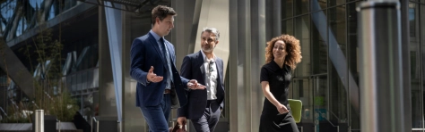 Three coworkers walking on city street with laptop discussing project