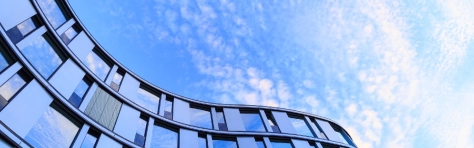 Detail of a modern office building in Hamburg, Germany. Professional services building seen from below, blue coloured glass windows with cloudy sky in the background.