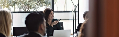 riunione con diverse persone e una businesswoman che sorride con computer davanti e penna in mano