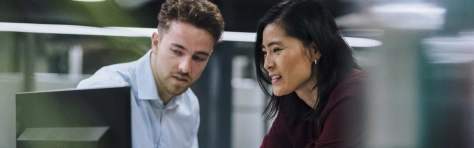 Young businessman discussing with colleague over desktop PC in office