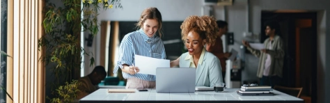 due donne che parlano ridendo davanti un computer ad una scrivania