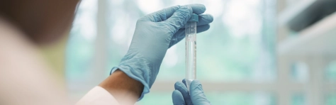 Virologist wearing blue rubber gloves, examining test tube while working in laboratory.