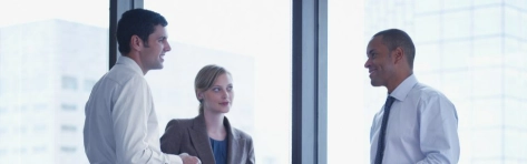 due colleghi e una collega che parlano tra loro in ufficio vetrato