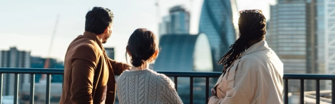 Multiracial business coworkers looking out across city at sunrise. Rear view of business people standing on rooftop in an office building against cityscape of London. Startup founders and partners looking to the br