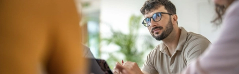 ragazzo con una penna in mano guarda ad un'altra persona di spalle con maglione giallo