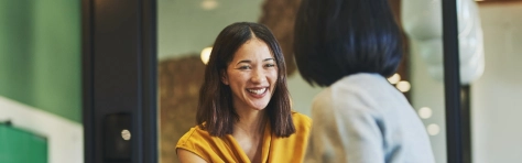 Two women greeting each other with a handshake in an office setting. Meeting between two young female professionals, with woman in yellow smiling.