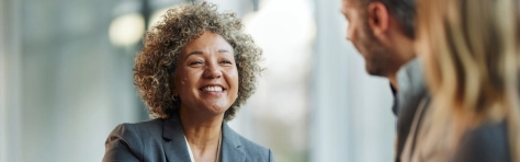 An image of a businesswoman smiling and looking at a man and woman