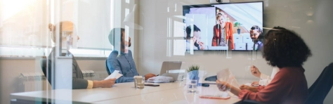 colleghi in riunione in una sala con uno schermo con collegamento da remoto