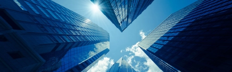 An aerial view looking up at the blue sky and three tall office buildings