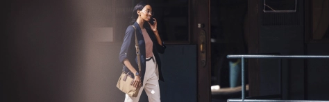 Confident businesswoman walking in the city while talking on the phone. Professional attire and urban setting convey a sense of purpose and activity.