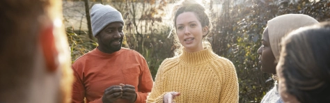 A multiracial group of volunteers wearing warm casual clothing and accessories on a sunny cold winters day. They are talking before they start working on a community farm, planting trees and performing other tasks.