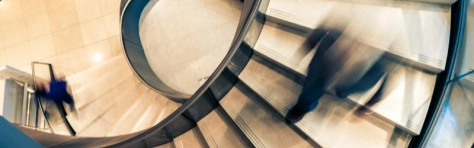 immagine dall'alto di una scala a chiocciola con delle persone sfocate che camminano sopra