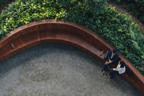 Ariel view of a man and a women talking on a long bench with bushes behind them