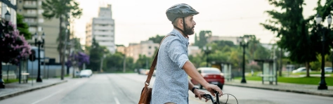 Man walking across city road on his bike with a bicycle helmet. Sustainable travel and eco friendly commute.