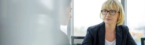 business woman con occhiali che guarda di lato ad una sua collega non ben visibile dato il riflesso