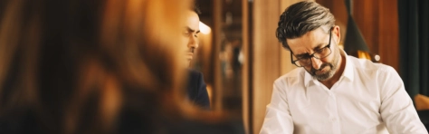 collega che scrive su un libro con accanto un altro collega che lo guarda e di spalle una donna