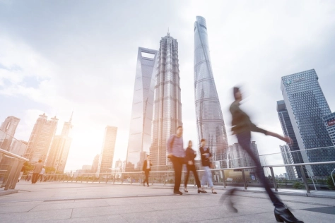 People that are blurred walking on a bridge with buildings behind them