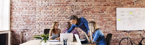 Image of a group of people sitting at a desk discussing and looking at a laptop