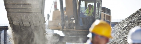 Man in hard hat blurred and man driving digger in background