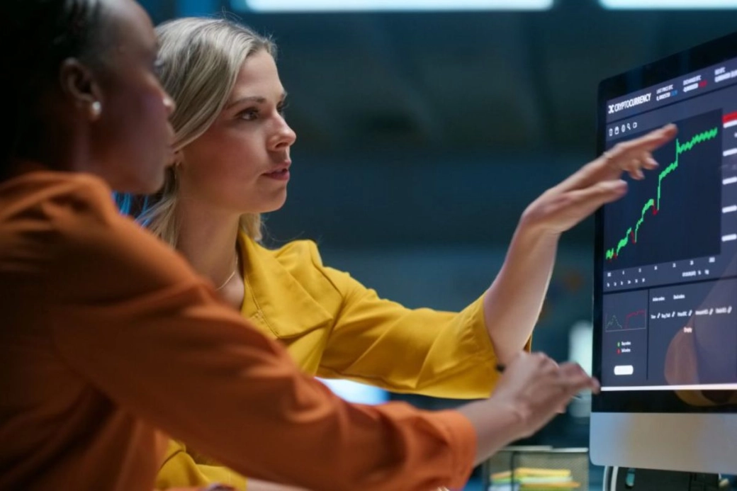 An image of two professional women looking at financial data on a computer screen.
