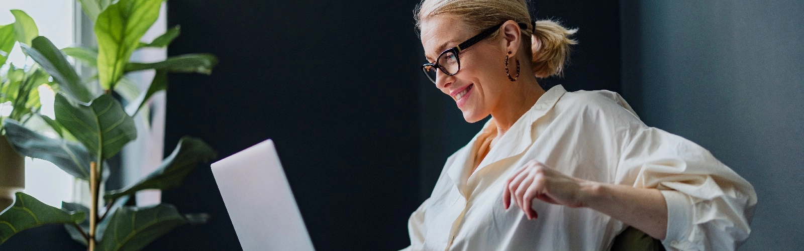 Wealthy woman wearing glasses sitting down on laptop at home, working on business and finances.