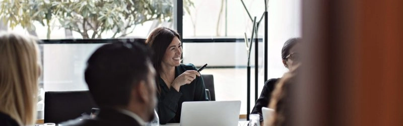 riunione con diverse persone e una businesswoman che sorride con computer davanti e penna in mano