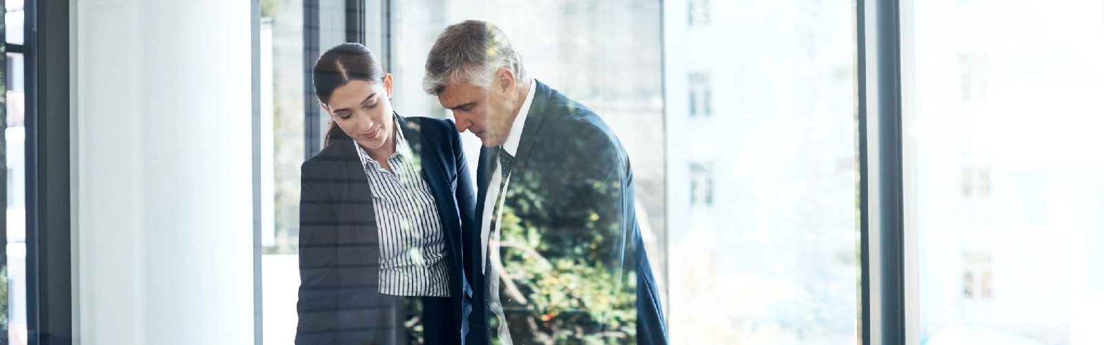 Shot of two professional business people having a discussion in an office in formal office wear. Man and woman are standing over a desk going over financial reports in modern office in city centre.