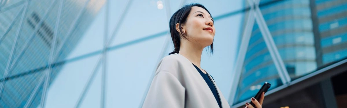 businesswoman che cammina in città con sfondo di un palazzo dietro e in mano un telefono