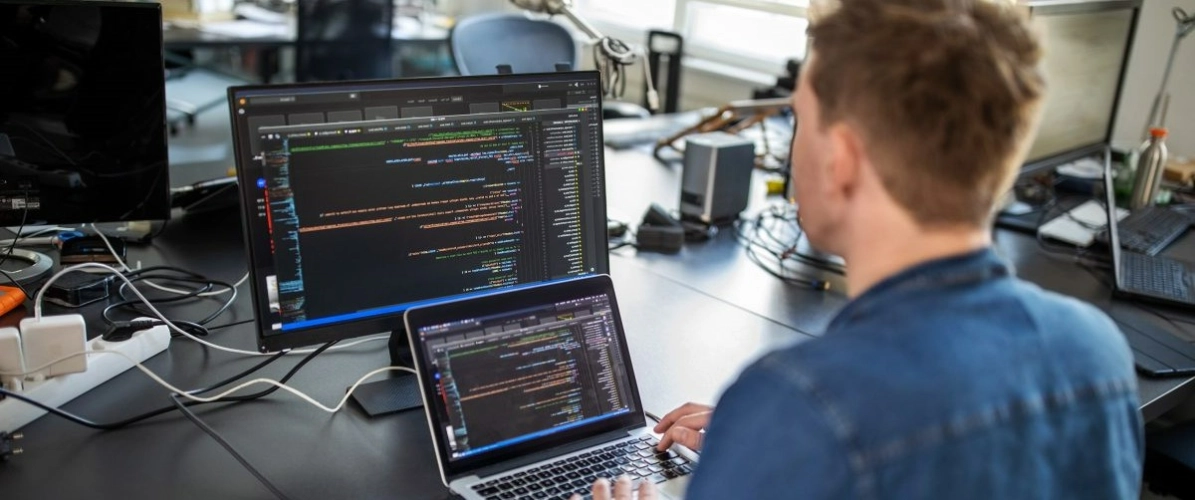 ragazzo con due schermi di computer davanti in cui sono presenti dei sistemi informatici