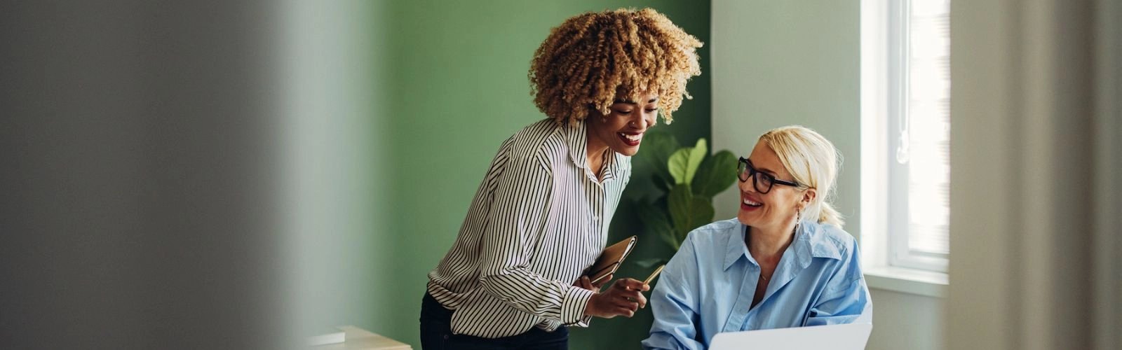 Two women discussing financial planning and taxes in a modern room with green walls and a plant in the background.