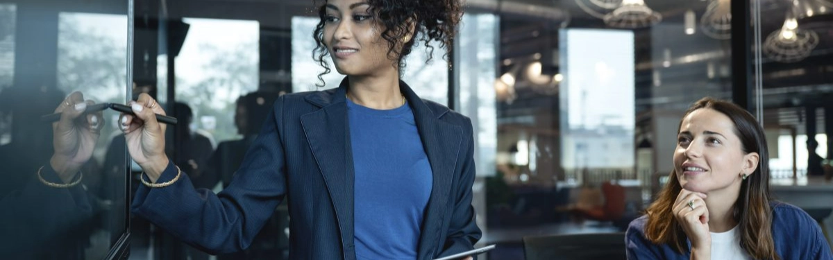 businesswoman disegna su una lavagna digitale con una collega che la ascolta